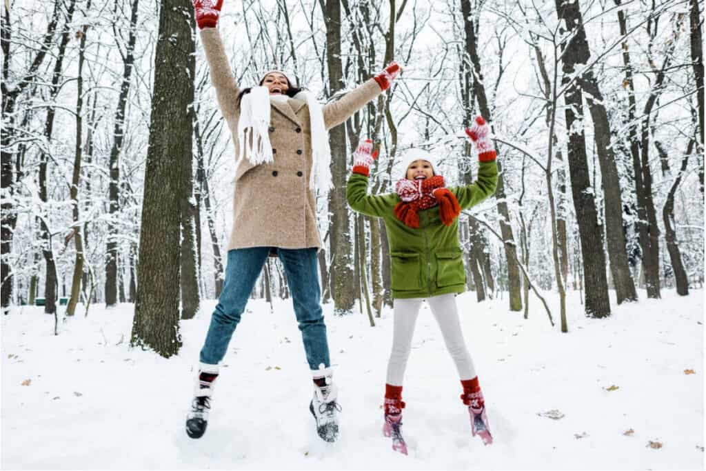 mom-and-daughter-jumping-in-snow-in-forest