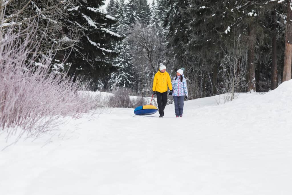 couple-walking-in-snow-with-tube-in-forest