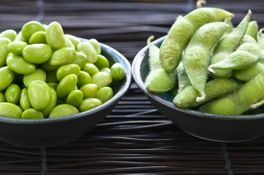 edamame (soy beans) in two bowls, one bowl with husks the other without