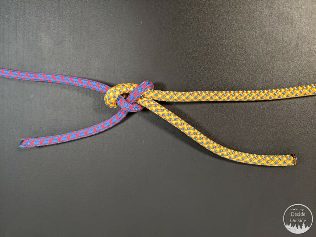 A sheet bend with a thicker yellow rope and a thinner blue and red rope