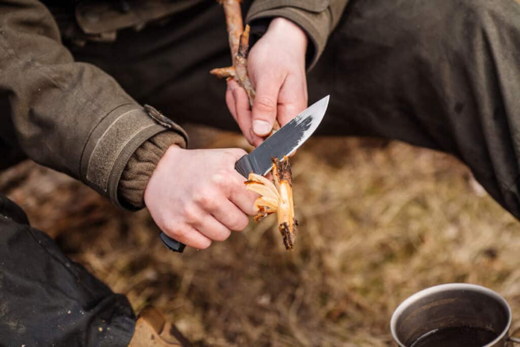 man using knife to peel back layers of bark of stick